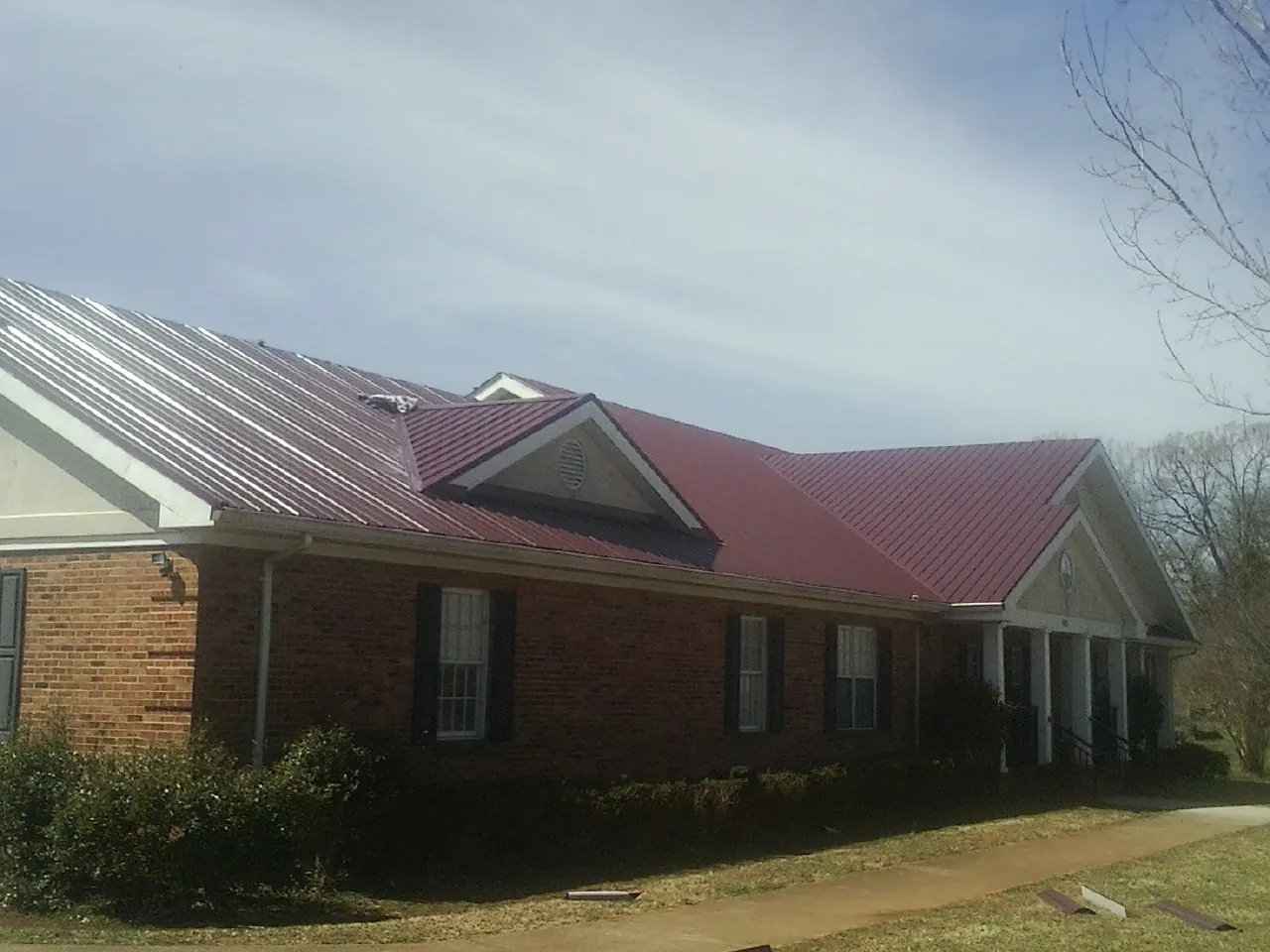 Red metal roof with gabled entries on a long brick building, from a Hail Damage Roof Repair job in Ace
