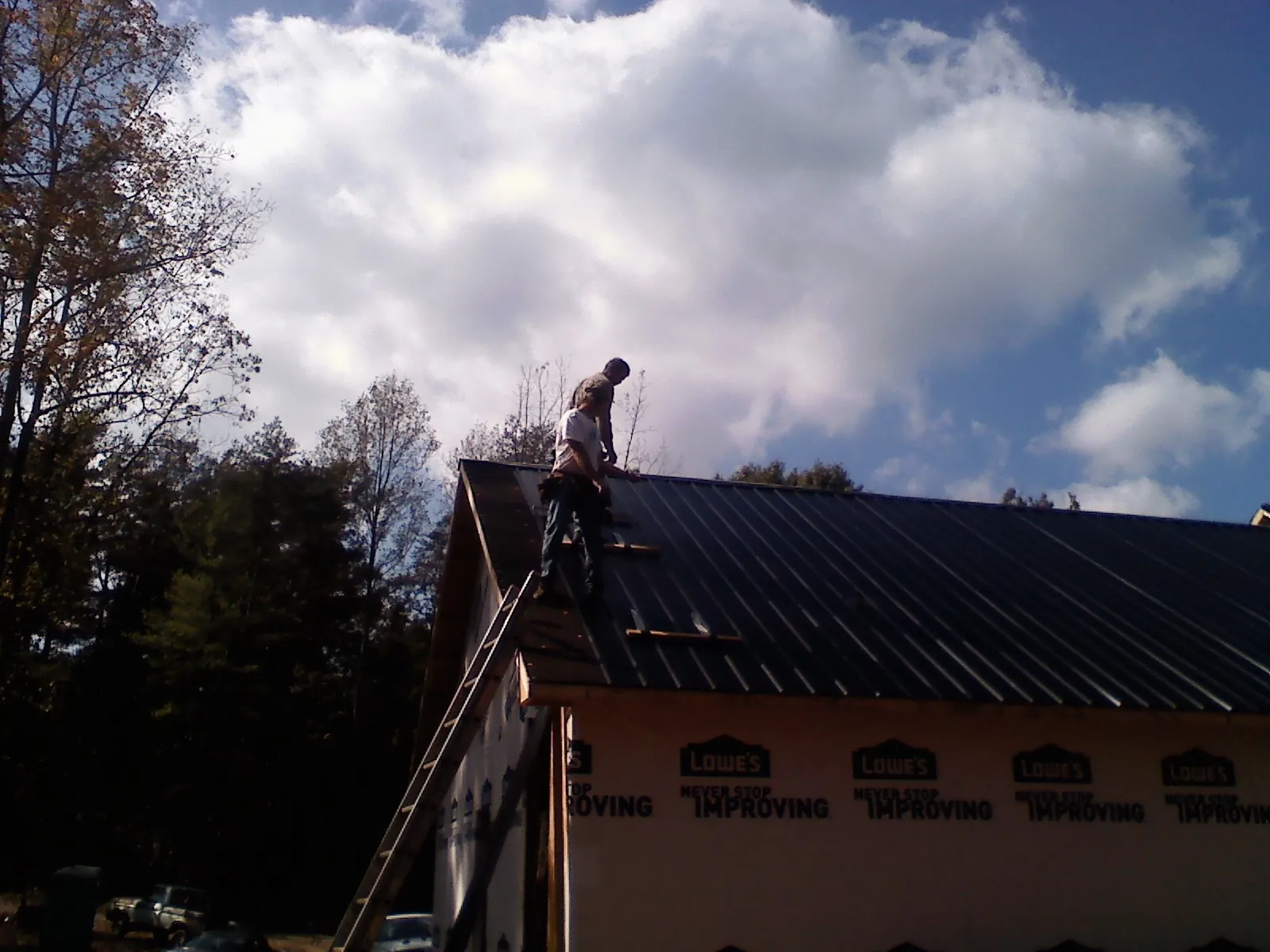 Roofer fastening dark metal panels high against a cloudy sky, from a Roof Inspection job in Ace