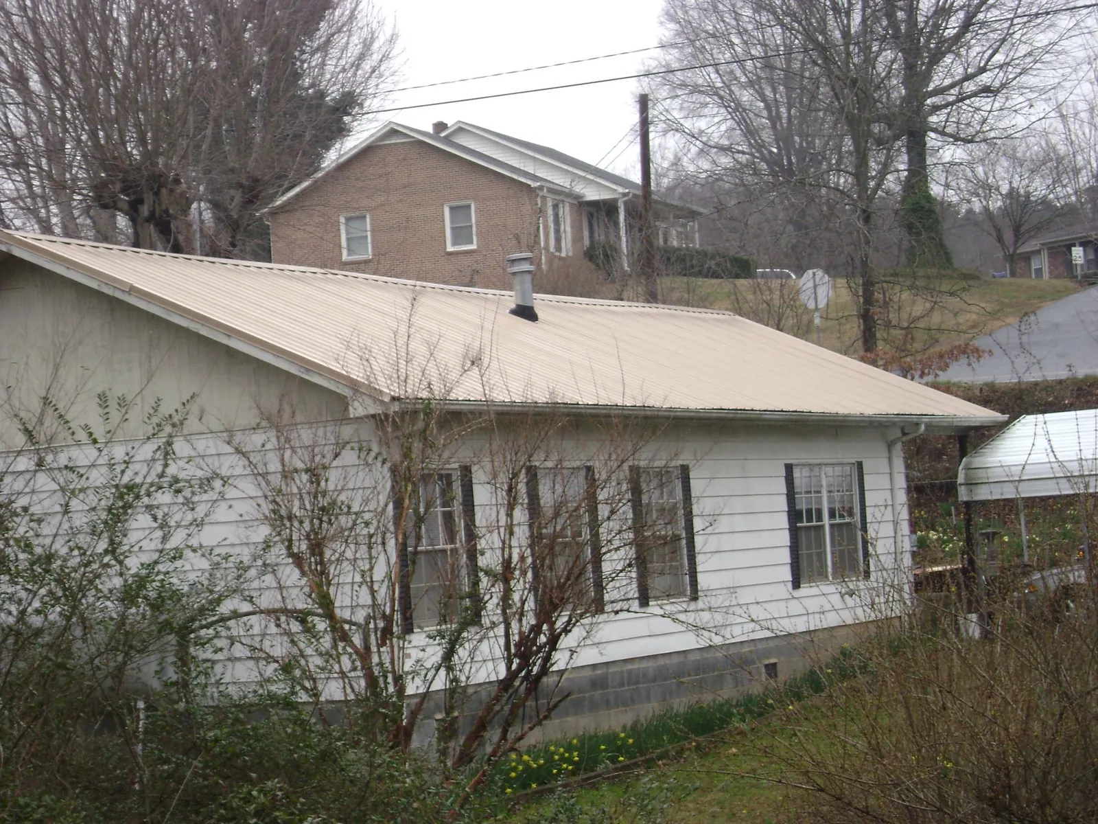 Tan metal roof on a white sided house set into a hillside — Commercial Roofing by Roofing Brothers in Ace