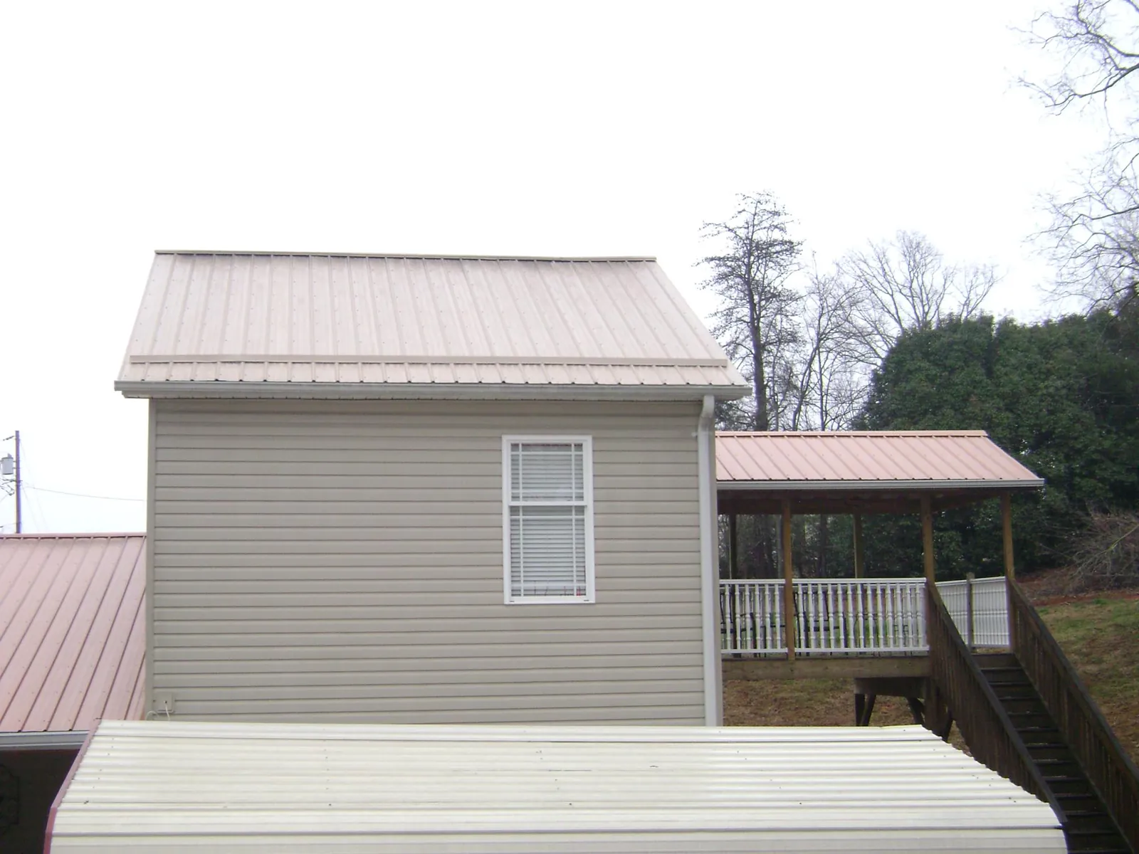 Tan metal roofs on a two story addition and attached porch, from a Roof Replacement job in Ace